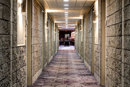 A hallway with patterned carpet, stone walls, and recessed lighting.