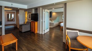 A hotel room with a living area, a television, a sofa, a wooden cabinet, a small table, and a bathroom with a bathtub and sink. - Grand Hotel & Conference Centre Calgary Airport, an Ascend Collection Hotel (Calgary)