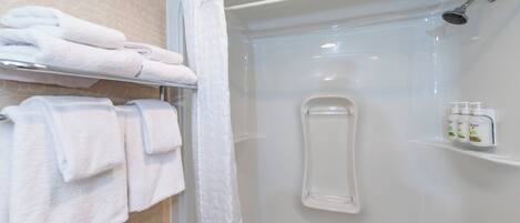Douchecel met een glazen deur, een handdoekrek met opgevouwen handdoeken en een plank met toiletartikelen.