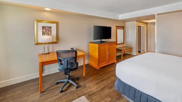 A hotel room with a bed, a desk with a chair, a television, a cabinet, and a framed picture on the wall.