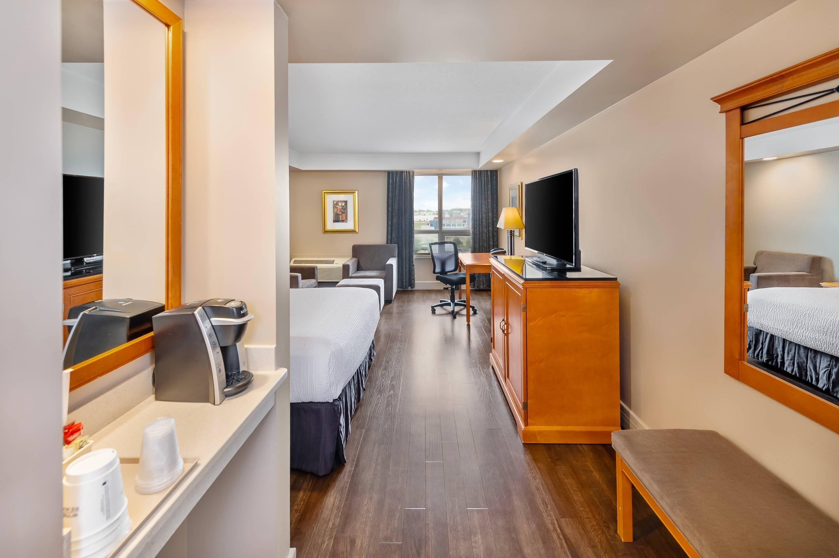 Habitación de hotel con cama, escritorio, silla, televisor, cafetera y ventana con vistas.