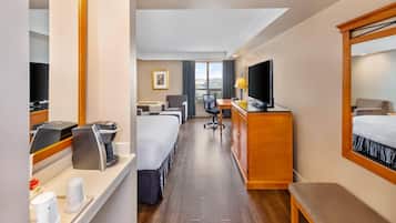 Habitación de hotel con cama, escritorio, silla, televisor, cafetera y ventana con vistas.