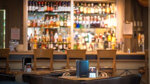 A bar area with a variety of liquor bottles on shelves, wooden chairs, and tables. - Grand Hotel & Conference Centre Calgary Airport, an Ascend Collection Hotel (Calgary)