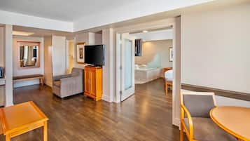 A hotel room with a wooden floor, a television, a sofa, a dining table, and a chair.