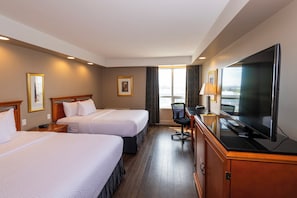 A hotel room with two beds, a desk with a TV, and a window with curtains.