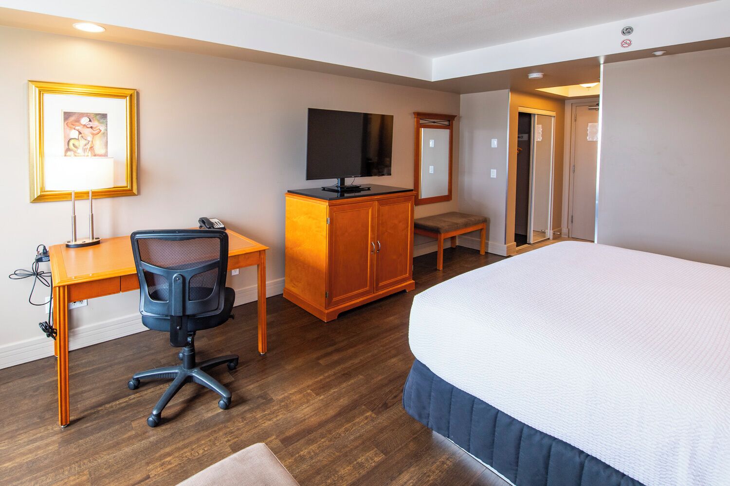 Habitación de hotel con cama, escritorio, silla, televisor y armario.