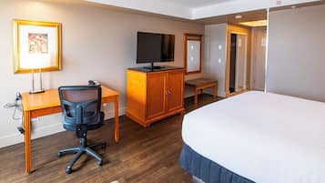 Habitación de hotel con cama, escritorio, silla, televisor y armario.
