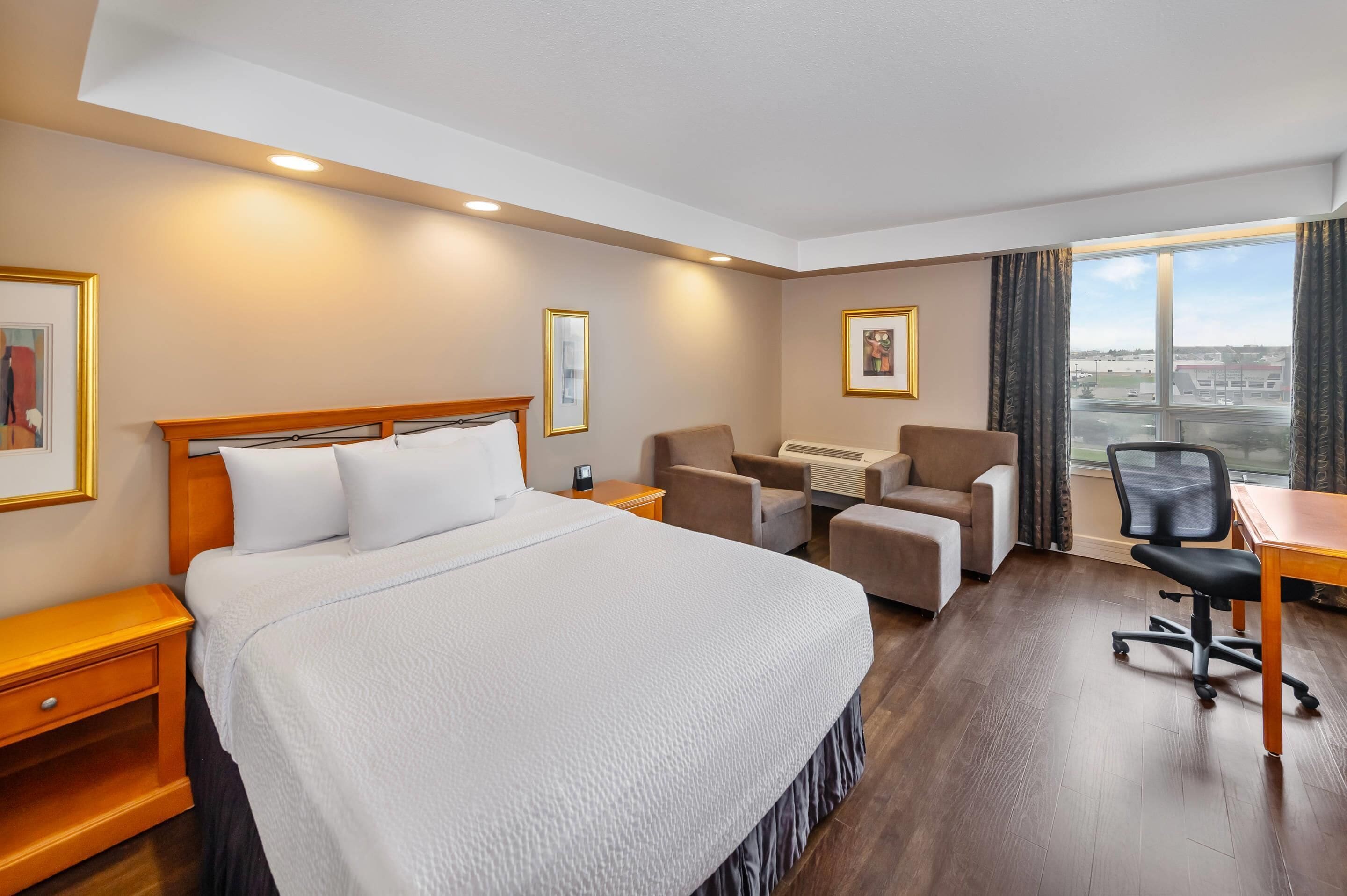 Une chambre d’hôtel avec un grand lit, un bureau, deux chaises, un radiateur et une fenêtre donnant sur un beau paysage.