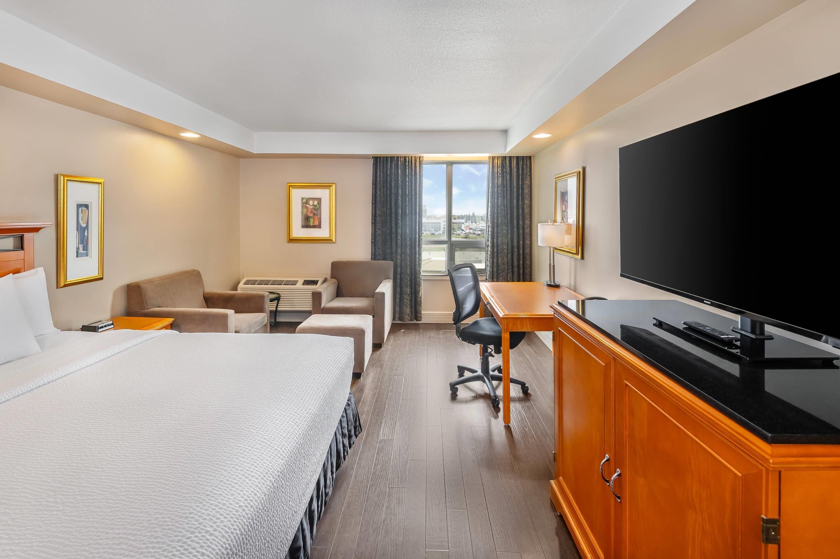 Una habitación de hotel con cama, escritorio, televisor de pantalla plana, sofá, sillón y ventana con cortinas.