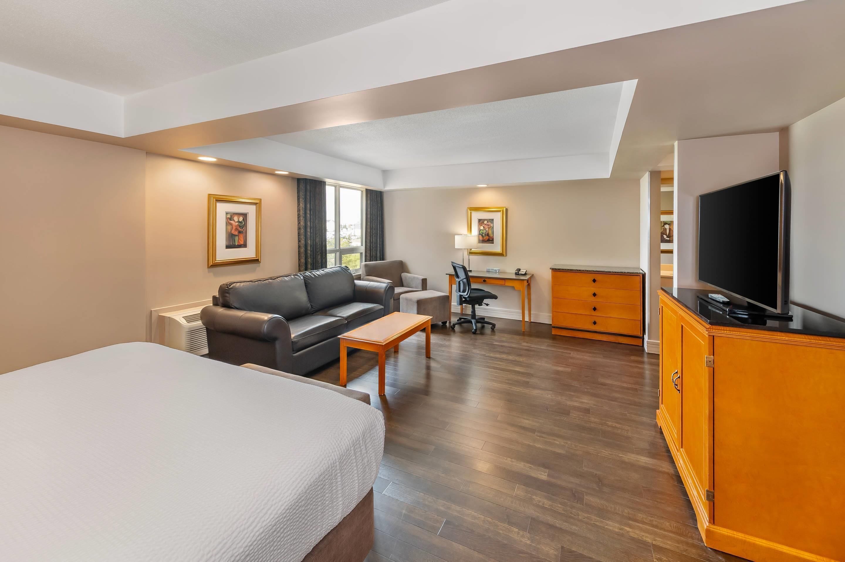 A hotel room with a large bed, a sofa, a desk with a chair, a television, and a wardrobe.