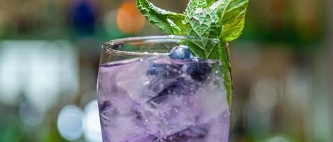 A tall glass with a purple drink, ice, and a mint leaf garnish.