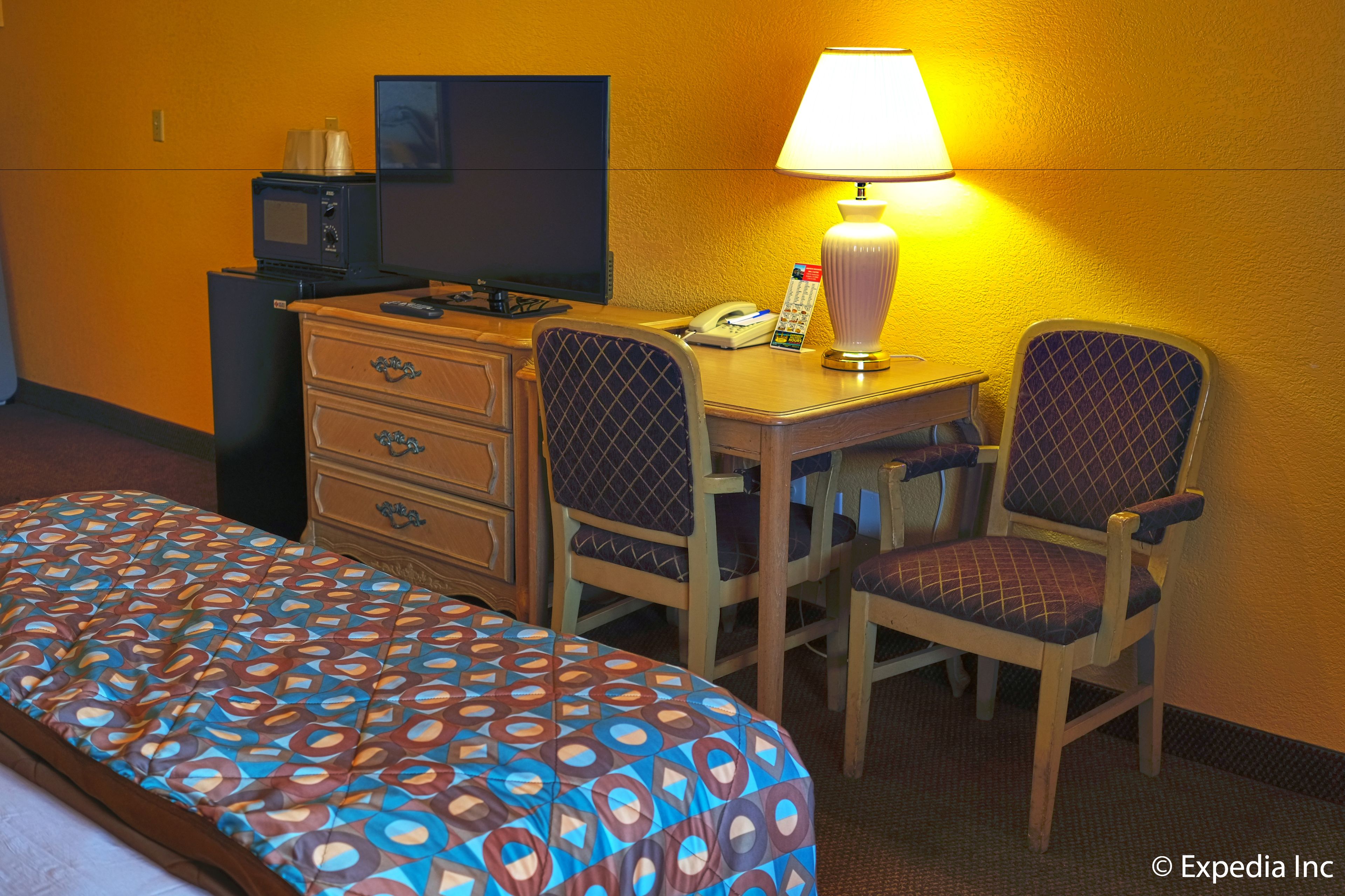 A hotel room with a bed, a desk with a lamp, a telephone, and two chairs.