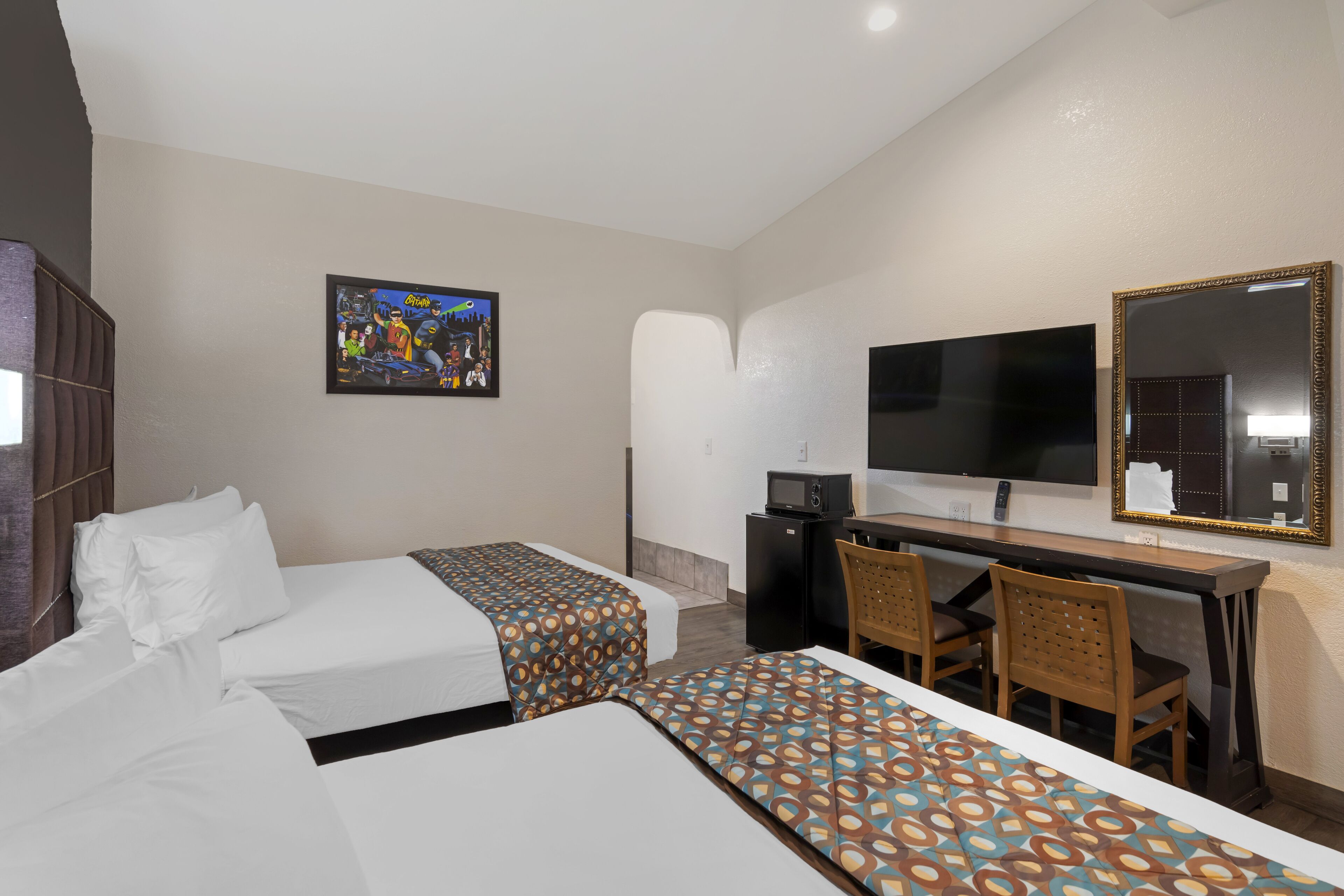 A hotel room with two beds, a desk with a chair, a TV, and a mirror.