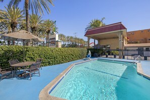 A swimming pool with lounge chairs and umbrellas, surrounded by palm trees and a building with a red roof. - Anaheim Discovery Inn & Suites (Anaheim)