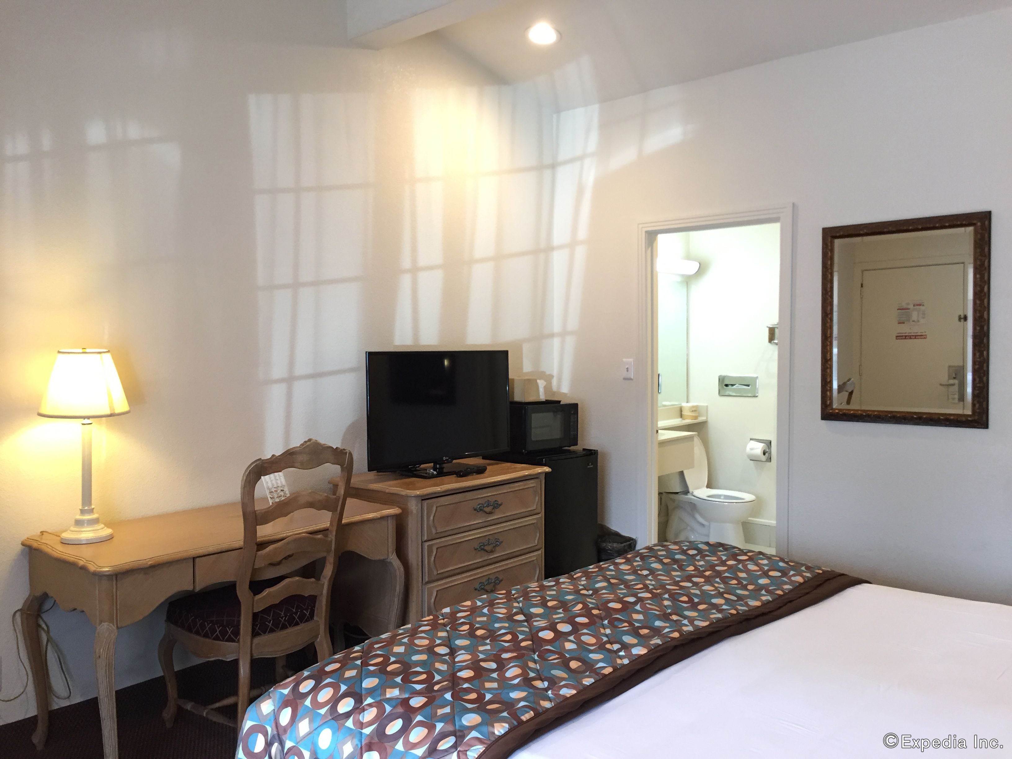 A hotel room with a bed, a desk with a computer, a chair, a TV, a microwave, and a mirror.