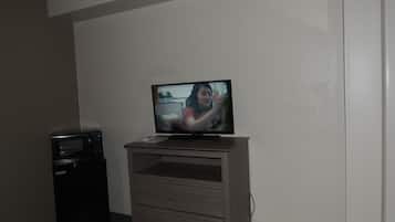 A room with a television on a wooden stand, a microwave, and a trash bin.