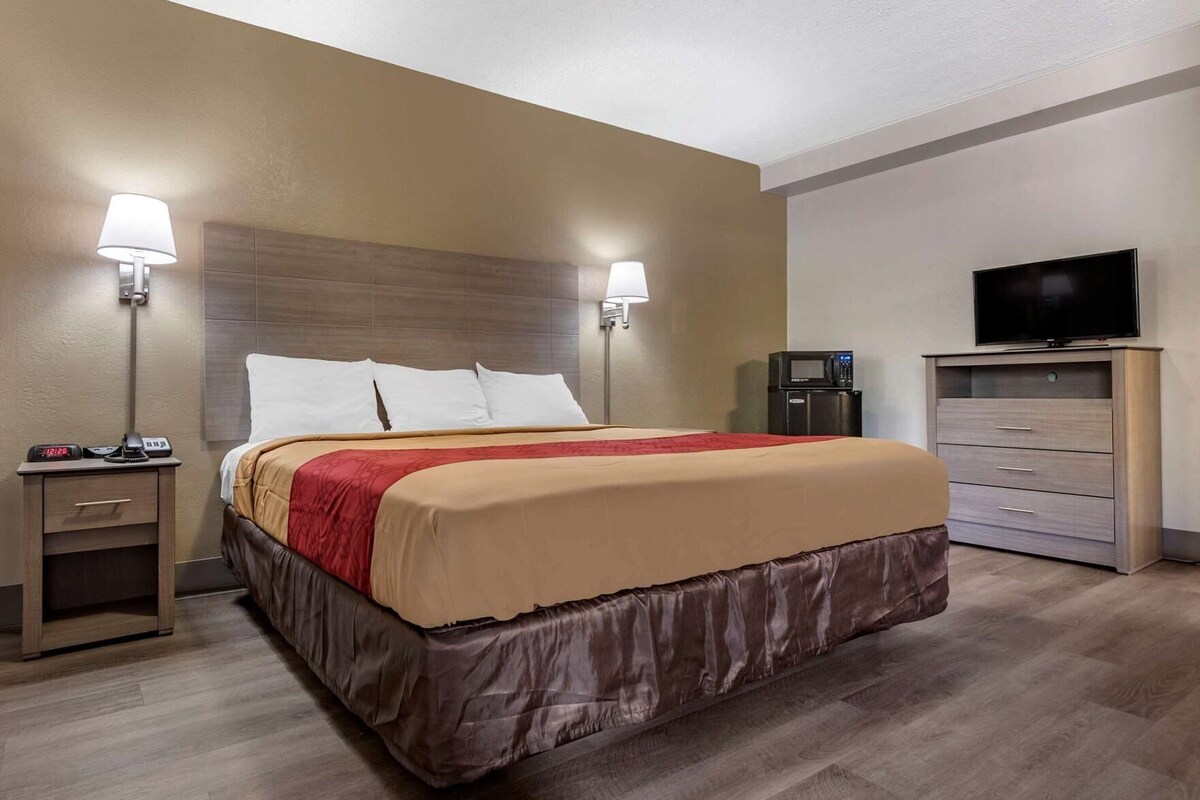 A hotel room with a bed, nightstand, lamp, TV, and a dresser.