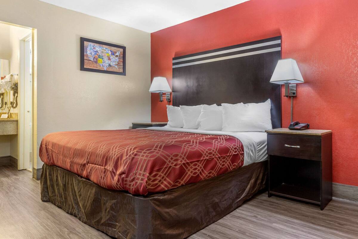 A hotel room with a large bed, red walls, two bedside lamps, a nightstand, and a framed picture on the wall.