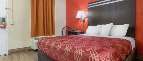 A hotel room with a bed, a nightstand, a lamp, a heater, and a door.