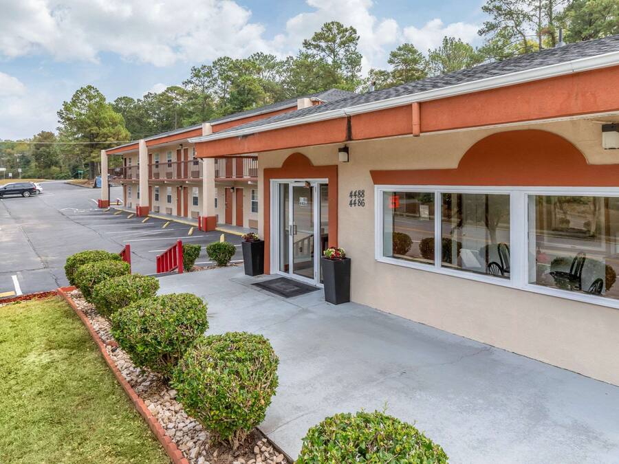 A motel with a parking lot, a drive-up window, and a small garden area with bushes and a fountain.