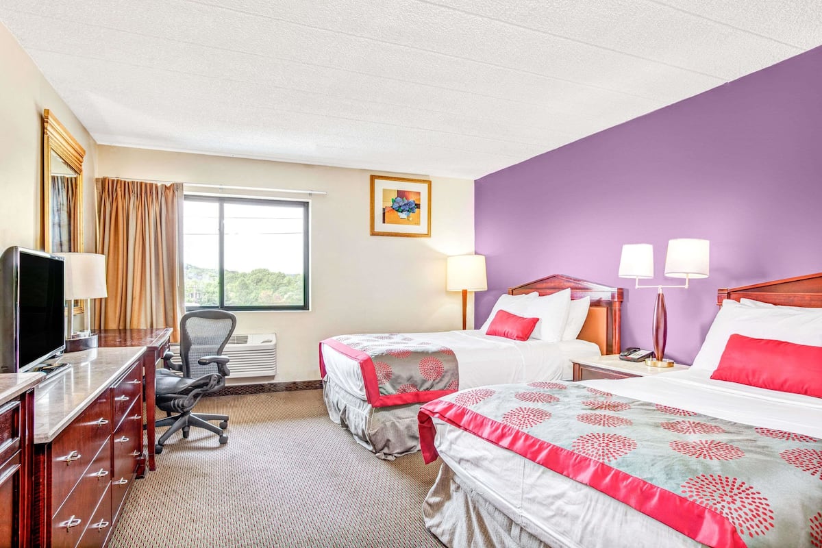 A hotel room with two beds, a desk with a computer, a chair, and a television.