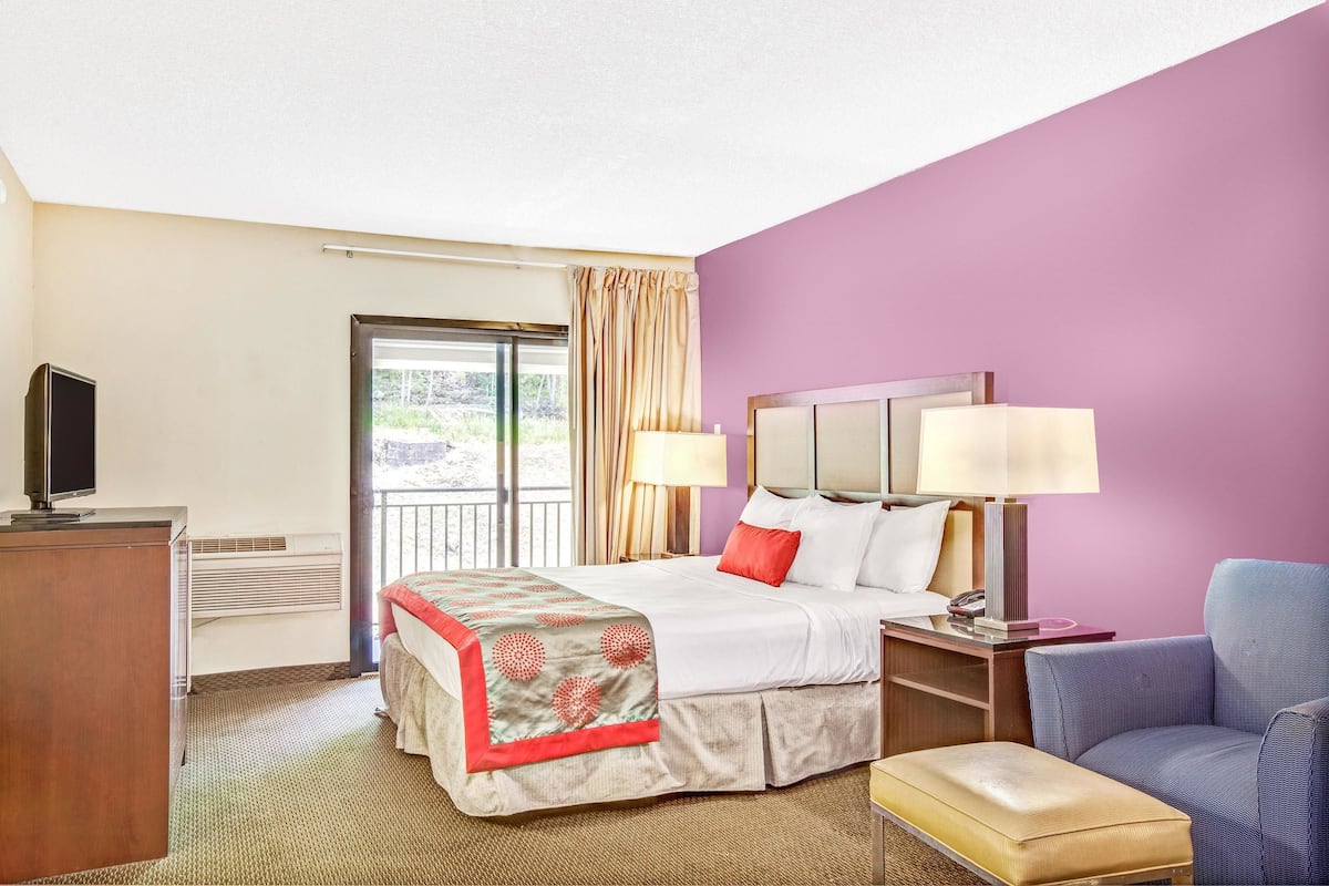 A hotel room with a bed, a desk with a computer, a chair, and a television.