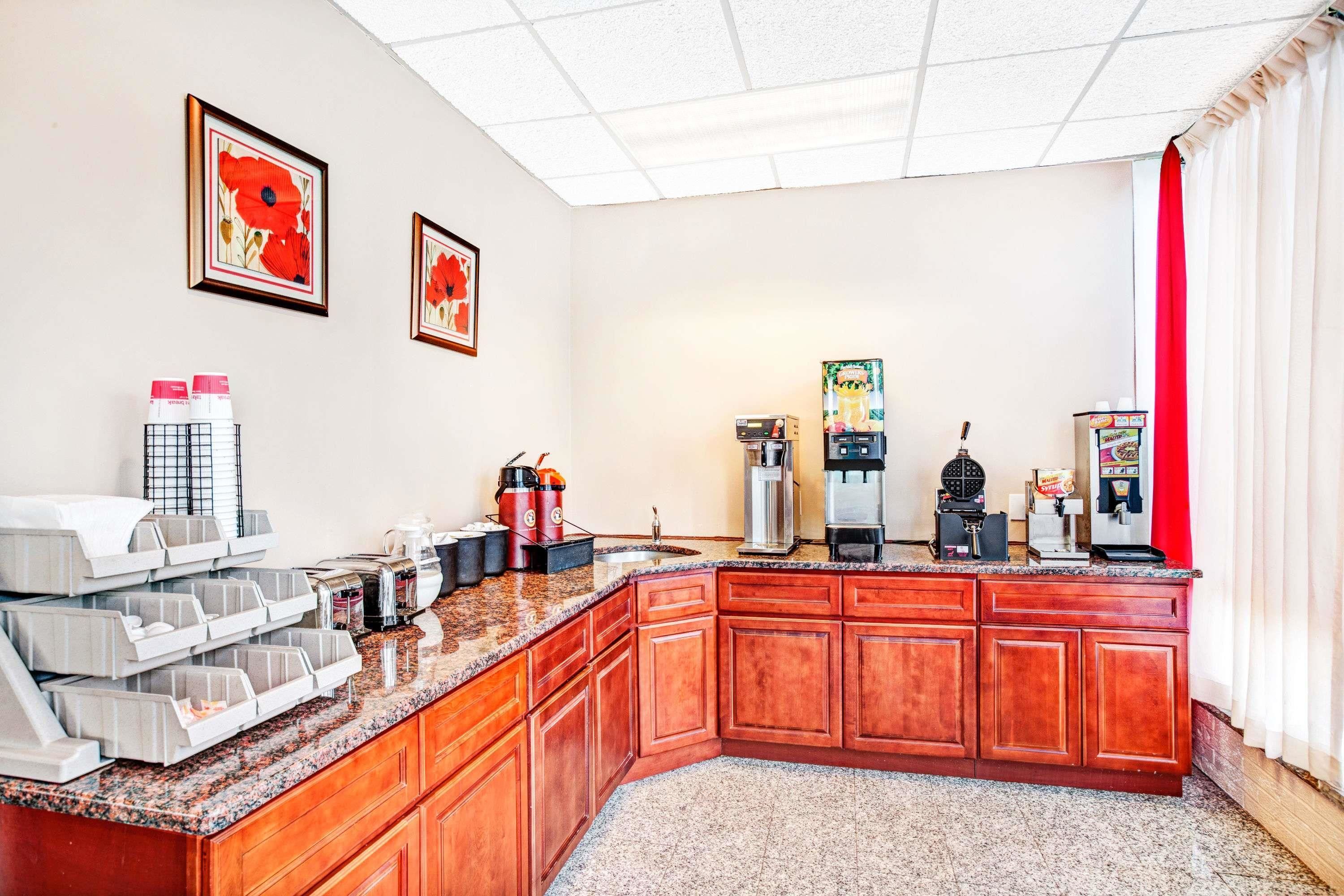 A hotel kitchen with a granite countertop, wooden cabinets, and various appliances including a coffee maker and a waffle maker.