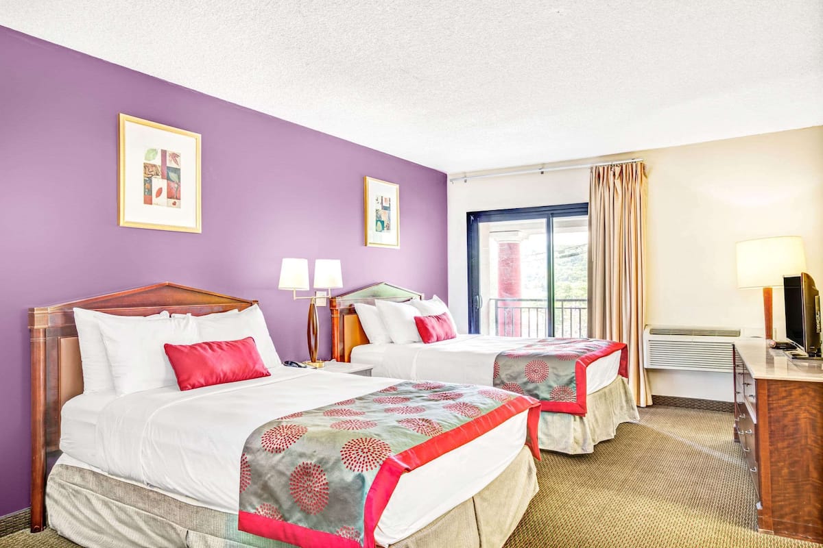 A hotel room with two beds, a desk, a TV, and two framed pictures on the wall.