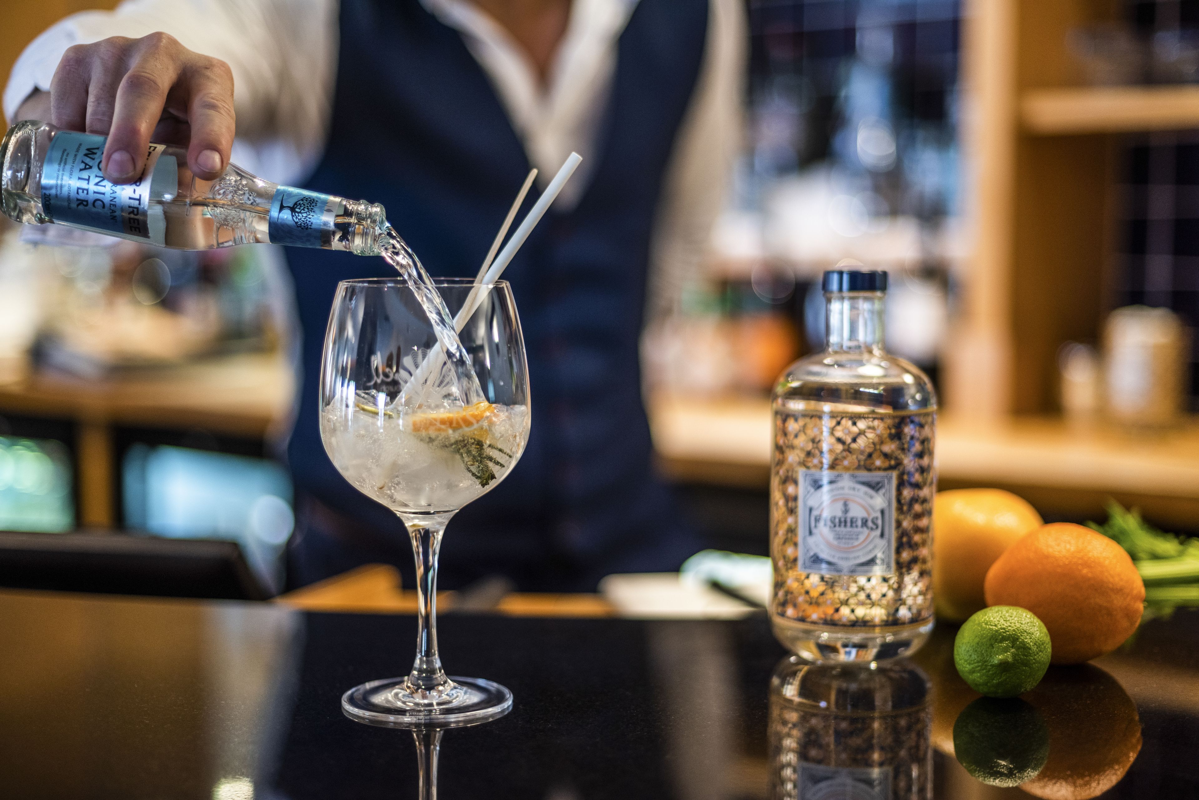 A bartender pouring a drink into a glass with a straw.