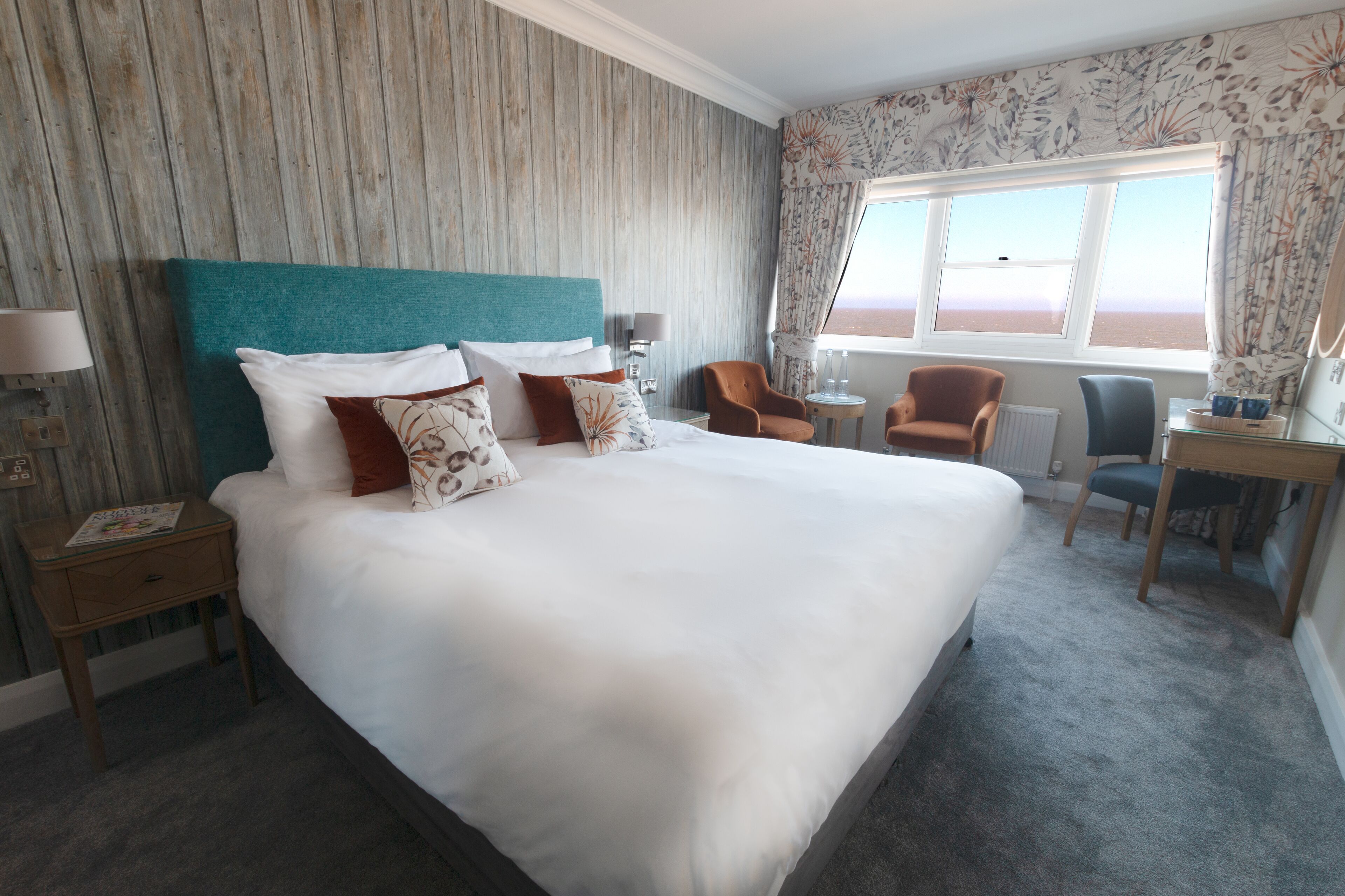 Habitación de hotel con una cama grande, un escritorio, dos sillas, una ventana con vistas y un cabecero de madera.