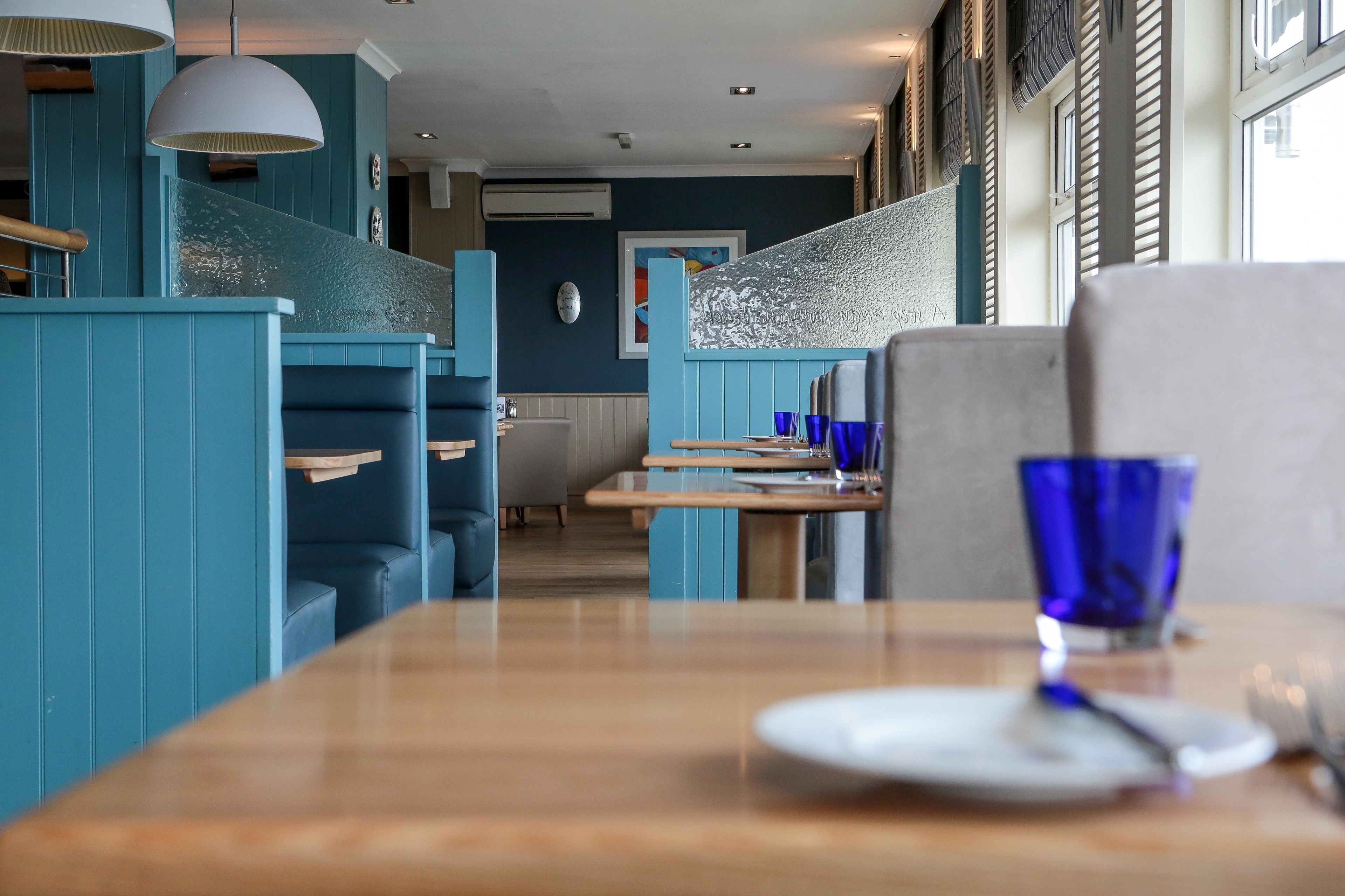 A restaurant with blue booths, wooden tables, and blue glassware.