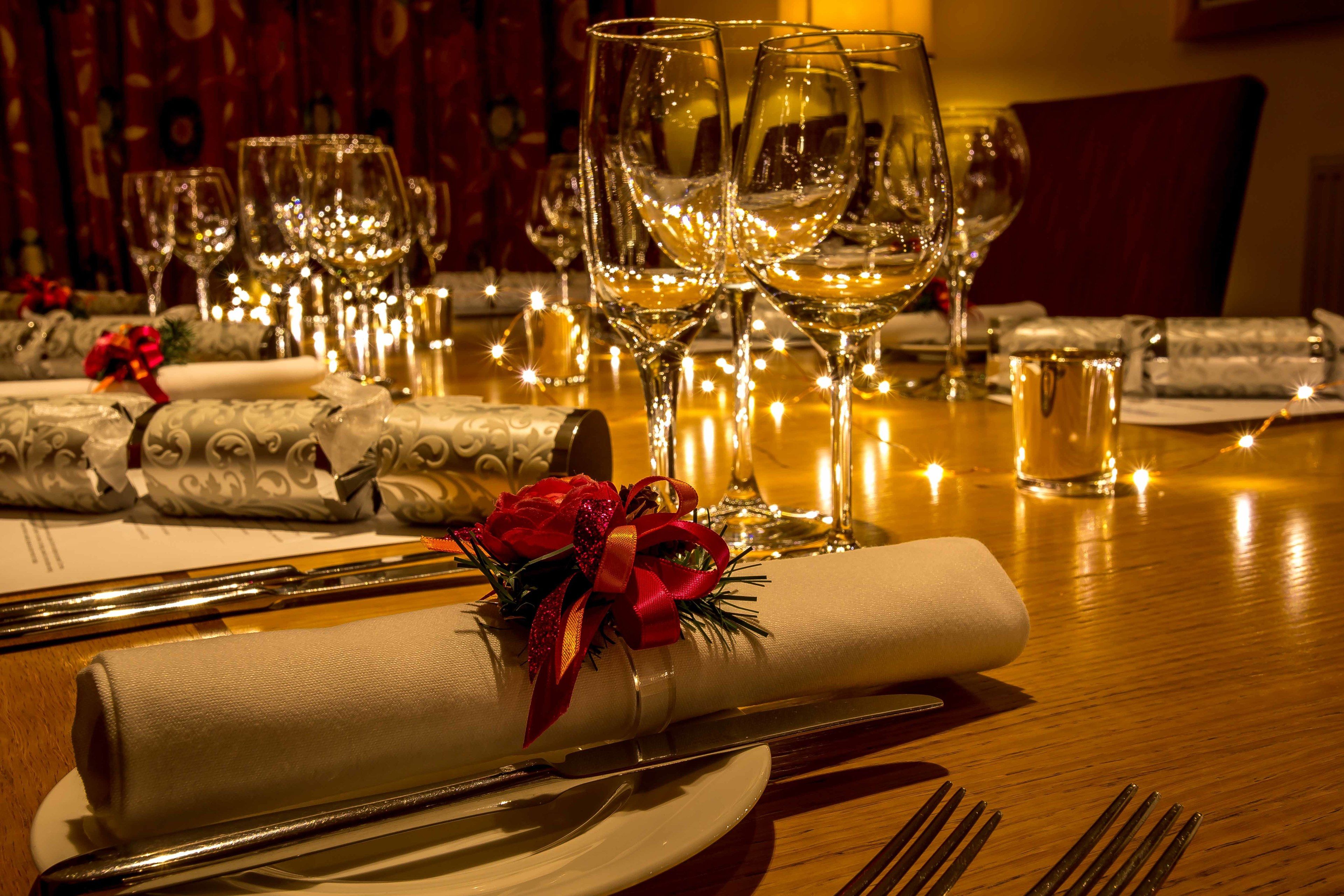 Una mesa dispuesta con copas de vino, un mantel doblado con lazo rojo y un cuchillo y un tenedor.