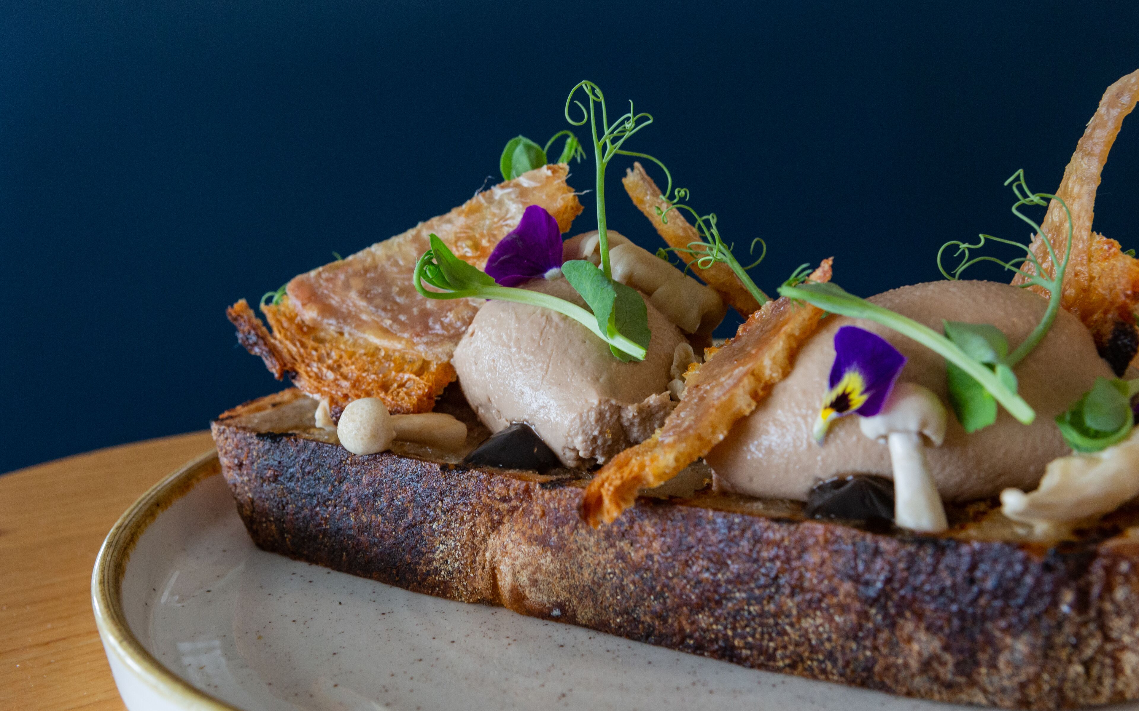 Une tranche de pain garnie d’un morceau de viande, d’une cuillerée de crème et décorée de verdure et de fleurs.