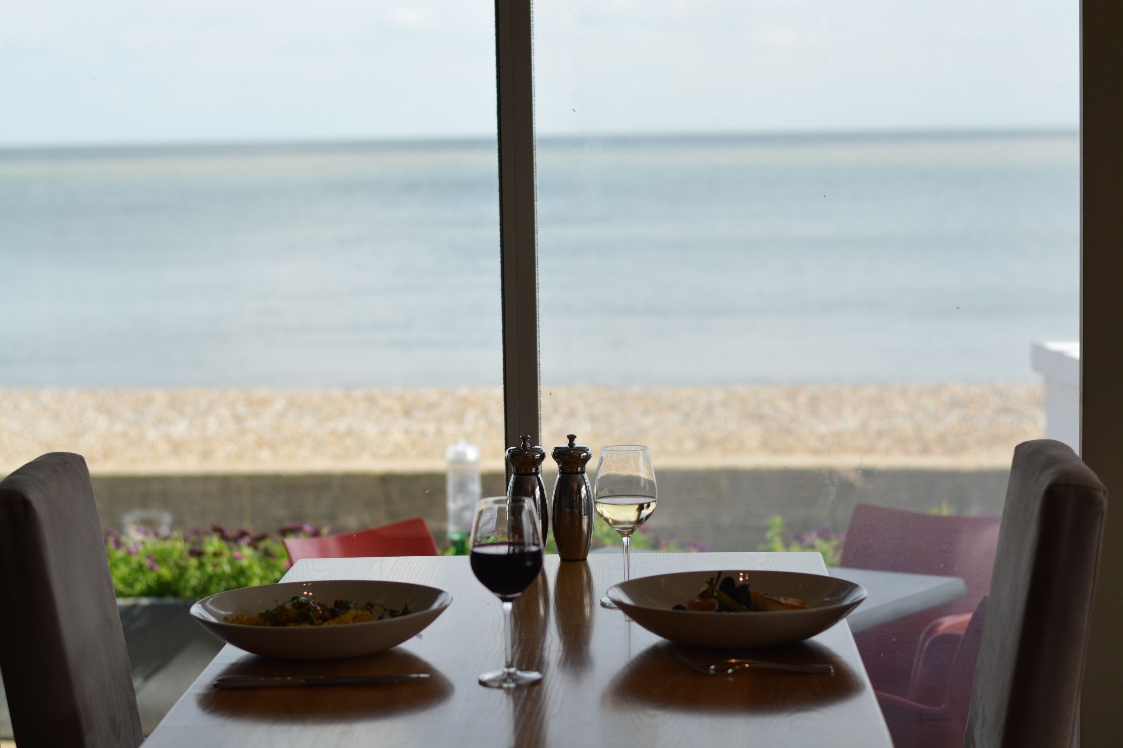 A table with two bowls, two glasses, and salt and pepper shakers, overlooking a beach.