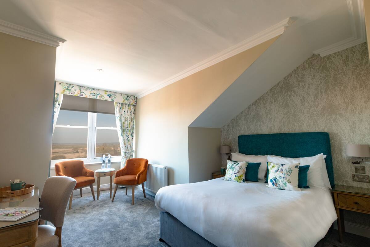 Un dormitorio con una cama grande, dos sillones, una mesita y vistas al exterior.