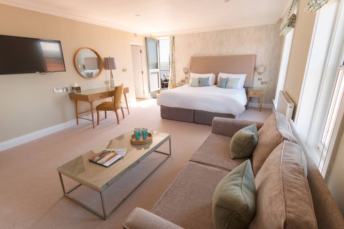 Habitación de hotel con cama, sofá, escritorio, televisor y balcón.