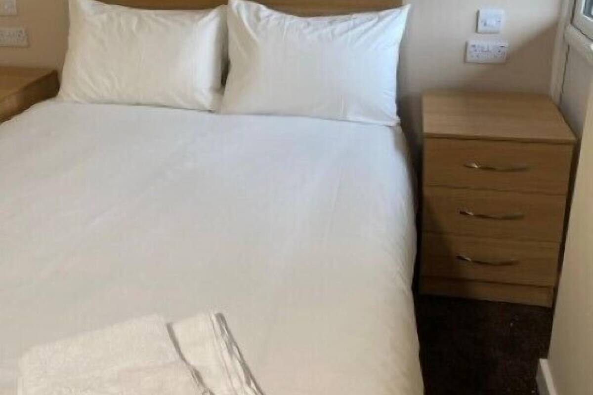 Hotelkamer met een groot bed, twee kussens, een nachtkastje met lades en een wandlamp.
