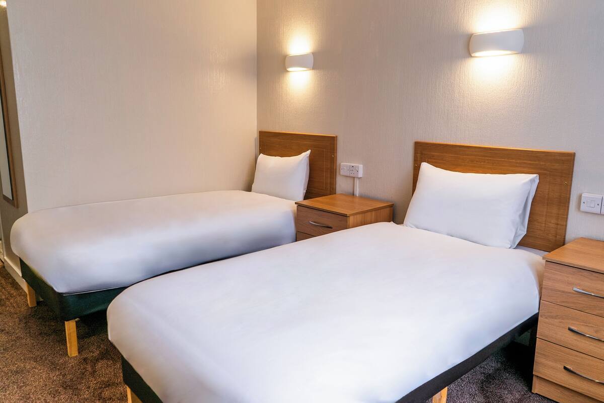 Een hotelkamer met twee enkele bedden, nachtkastjes en wandlampen.