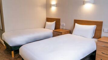 Habitación de hotel con dos camas individuales, mesitas de noche e iluminación empotrada.