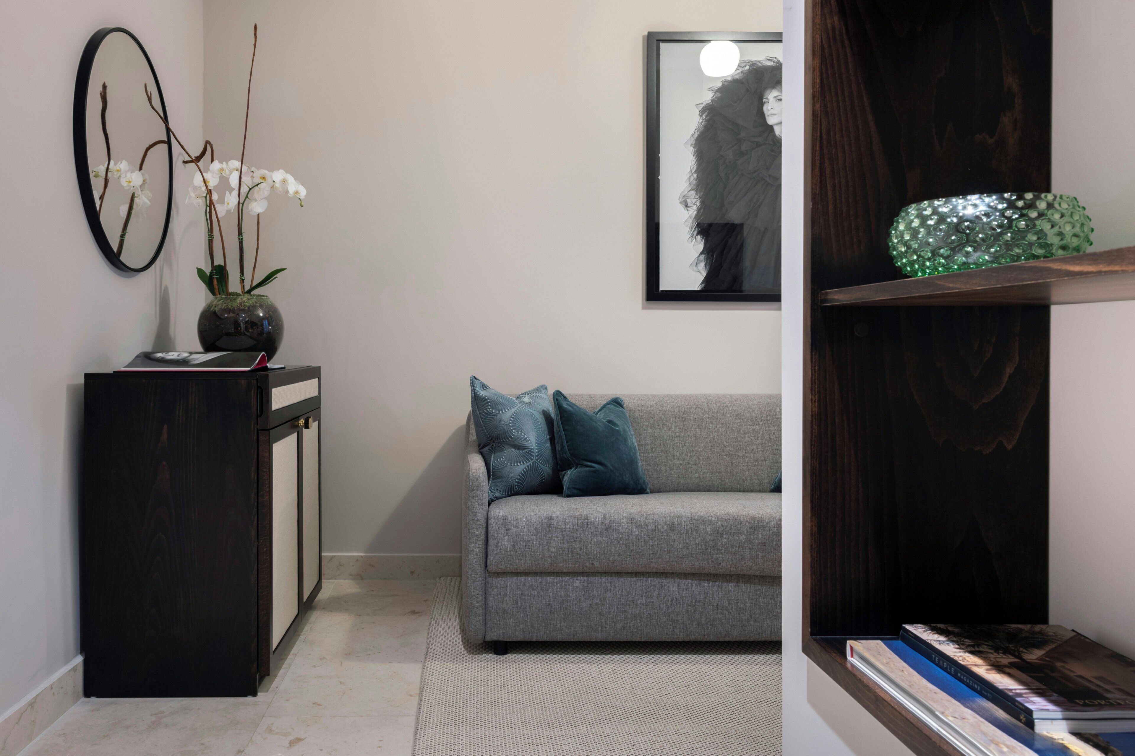 A modern living room with a grey sofa, a dark wooden cabinet, a vase with white flowers, and a framed artwork on the wall.