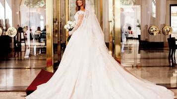 A bride in a white wedding dress standing at the entrance of a hotel with a red carpet.