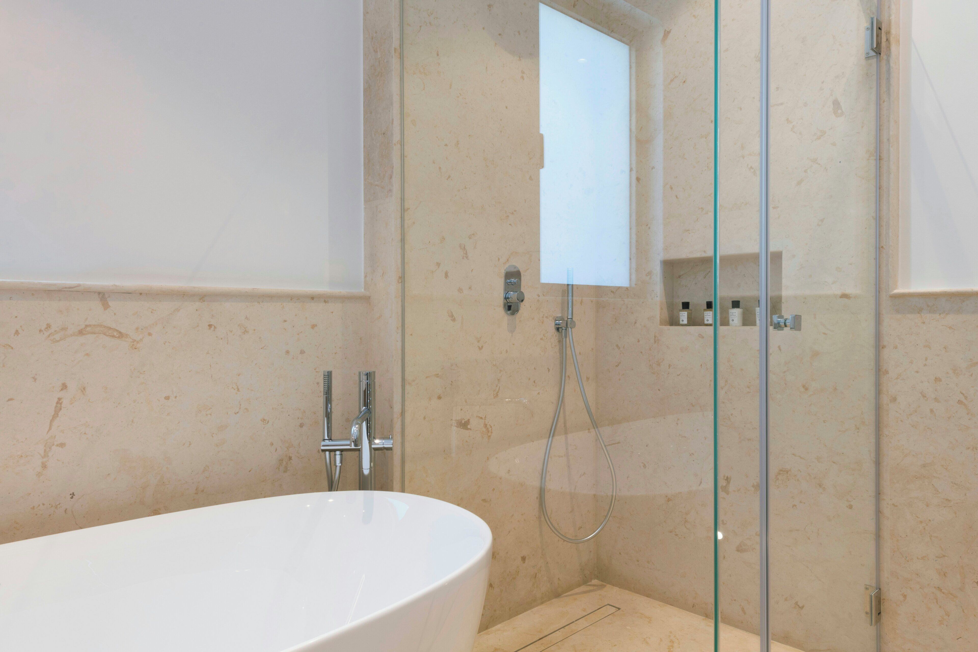 A bathroom with a freestanding bathtub, a glass-enclosed shower, and a marble wall.