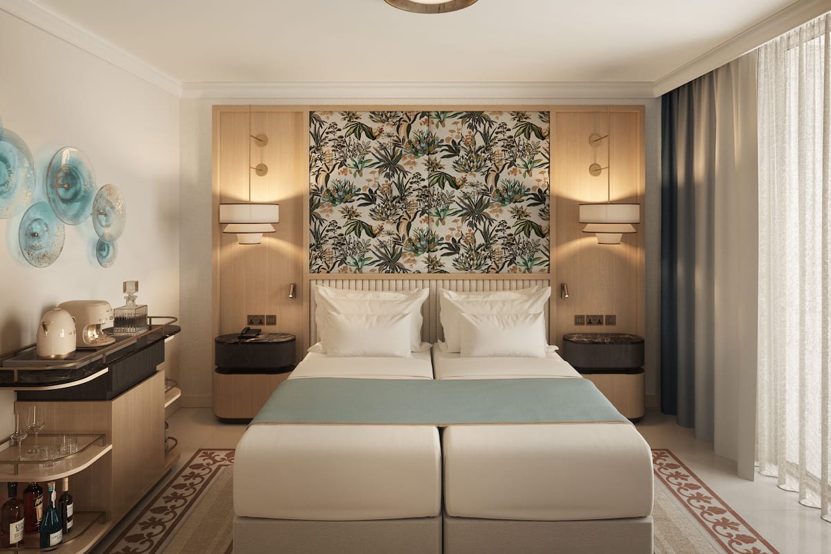 A hotel room with a bed, bedside tables, a nightstand, a decorative wall, and a window with curtains.