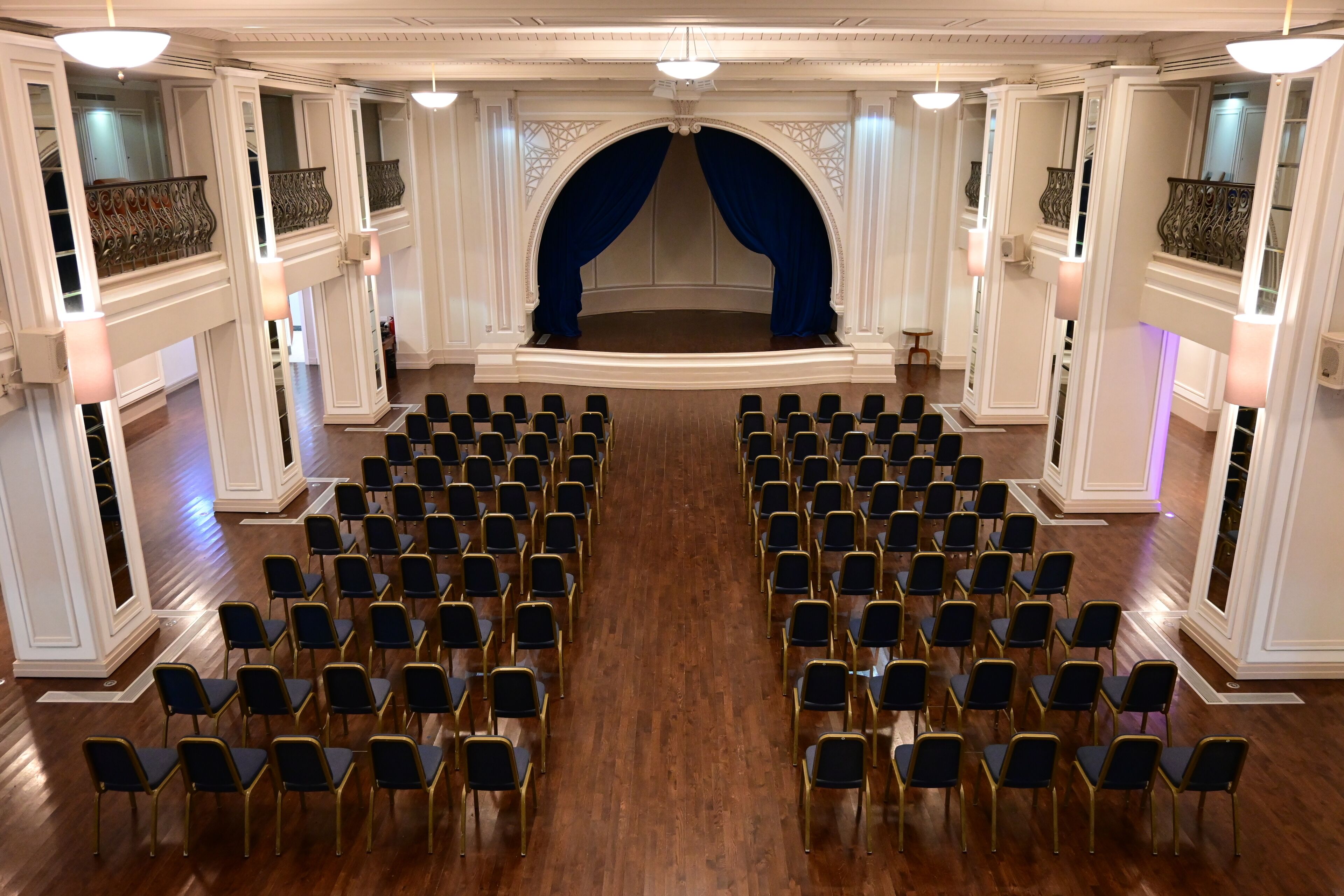 Un teatro con hileras de sillas orientadas hacia un escenario con un telón azul.