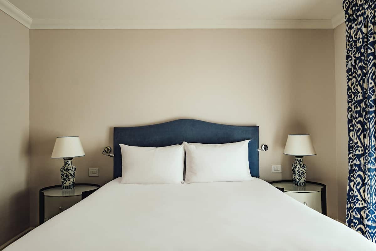 A bed with a blue headboard, two bedside tables with lamps, and a patterned curtain.