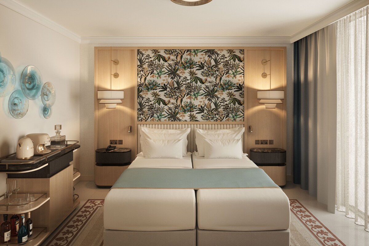 Habitación de hotel con cama, mesitas de noche, un ventanal con cortinas y un detalle decorativo en la pared.