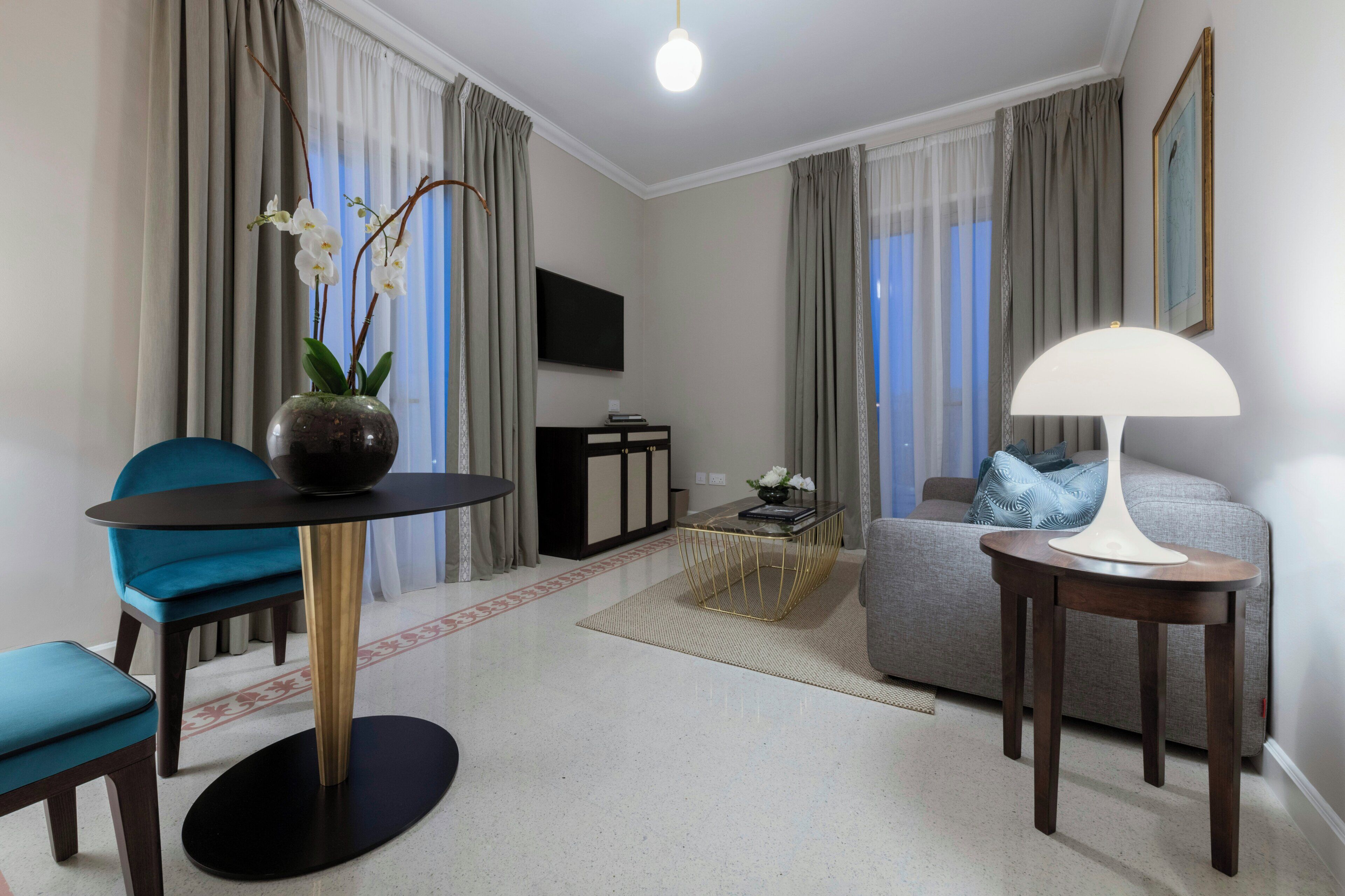 A modern living room with a round table, blue chairs, a sofa, and a TV.