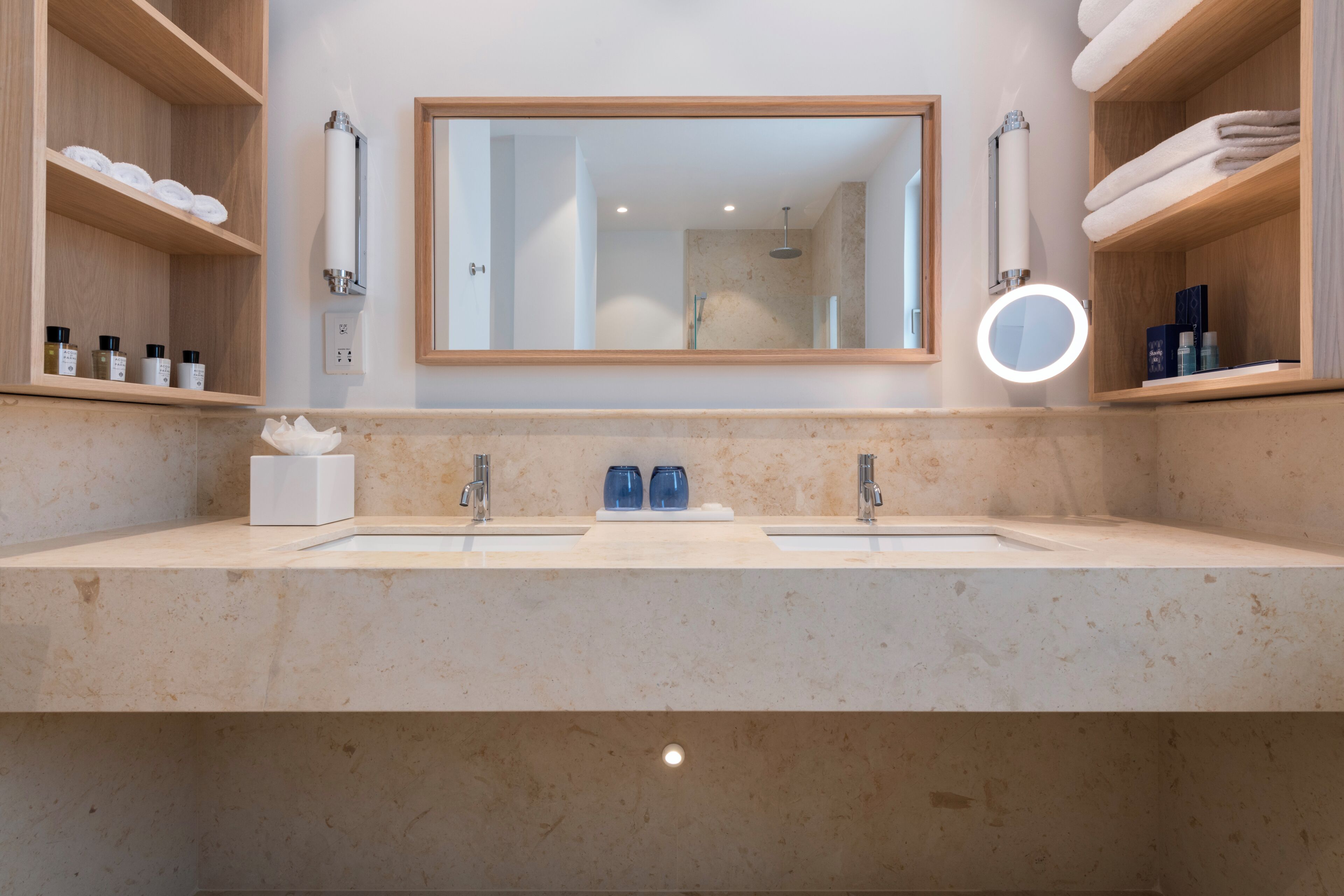 A bathroom with a double sink, a large mirror, and shelves with toiletries.