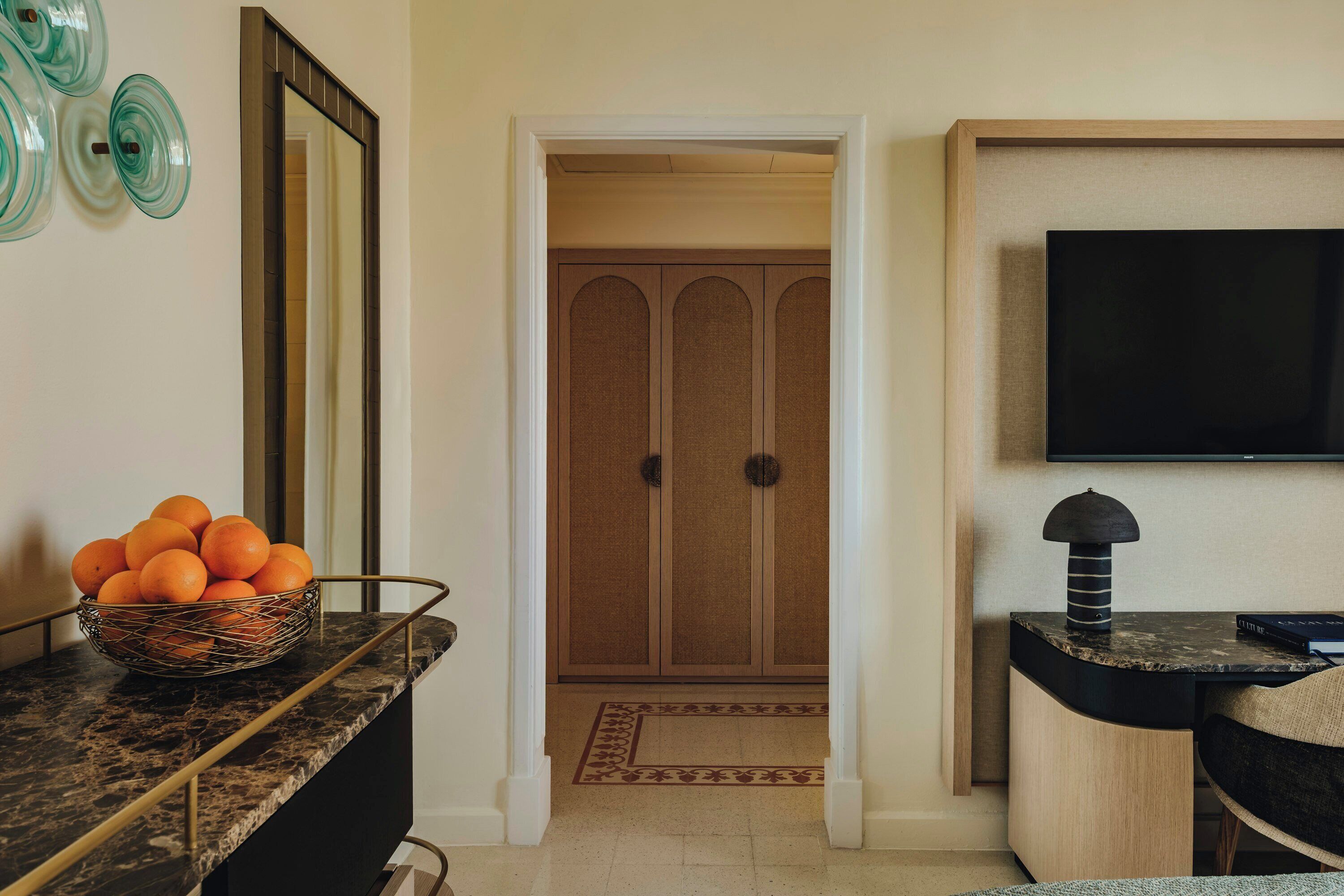 A room with a marble countertop, a bowl of oranges, a television, and a wooden wardrobe.