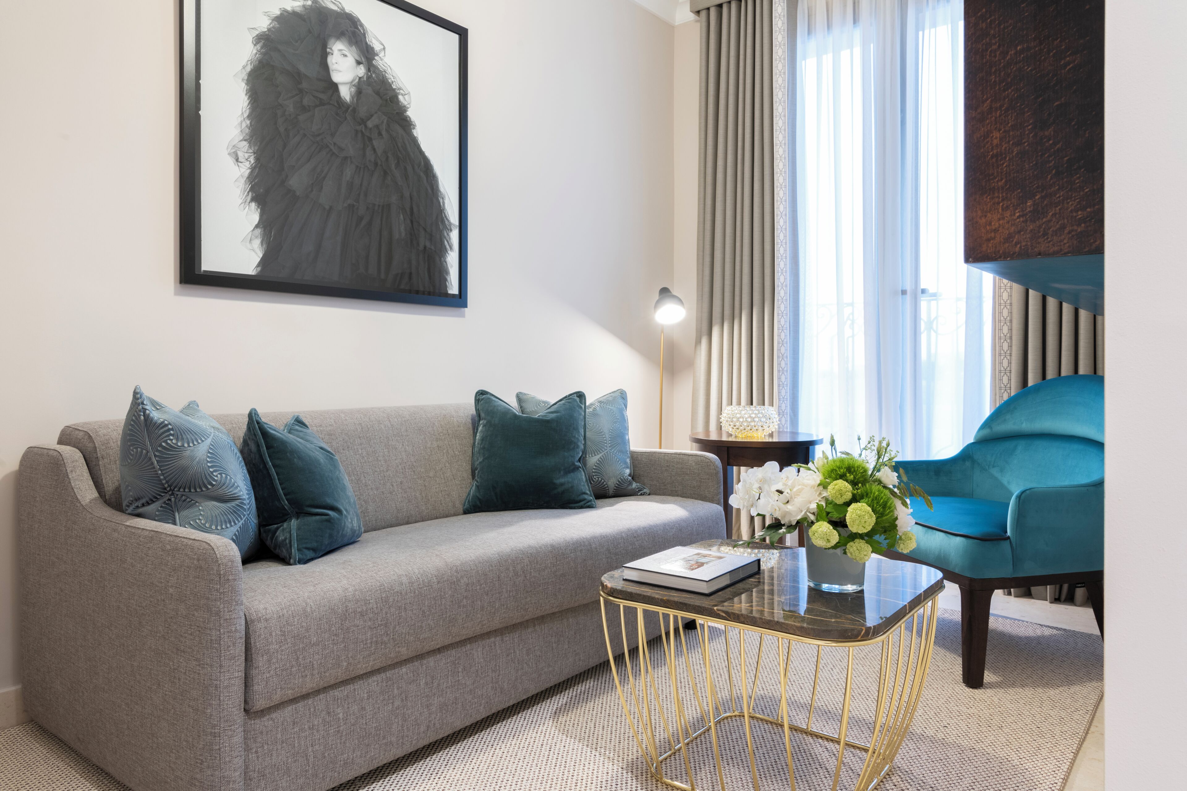 Una sala de estar con un sofá gris, un sillón azul, una mesa de centro y una obra de arte enmarcada en la pared.